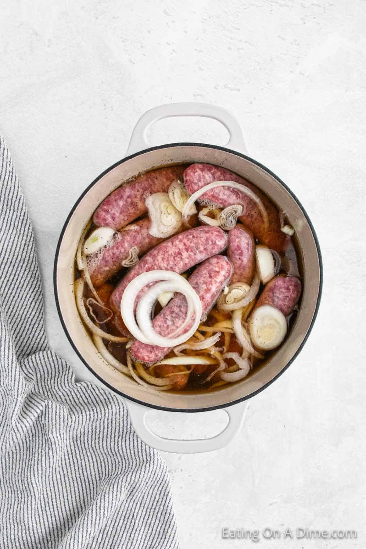 Raw brats in a large pot with beer and onions