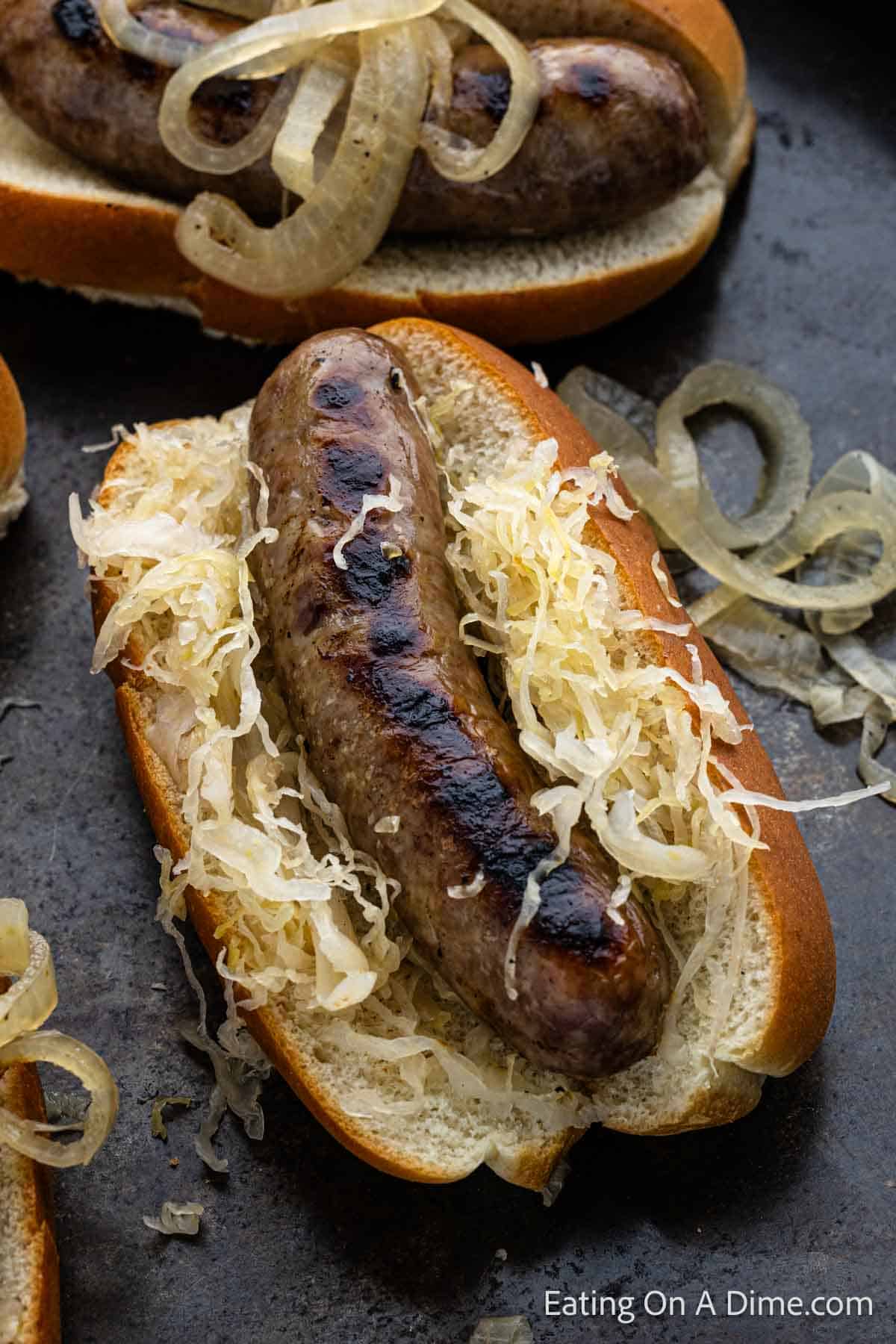 Grilled brats on a bun with sauerkraut on a plate