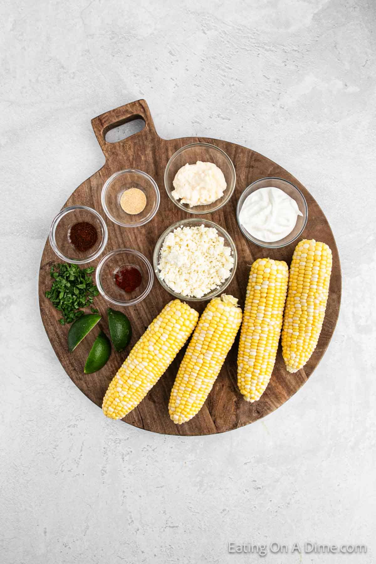 Mexican Corn on the Cob ingredients, corn on the cob on a platter with lime wedges, mayo, cheese, sour cream, seasoning 