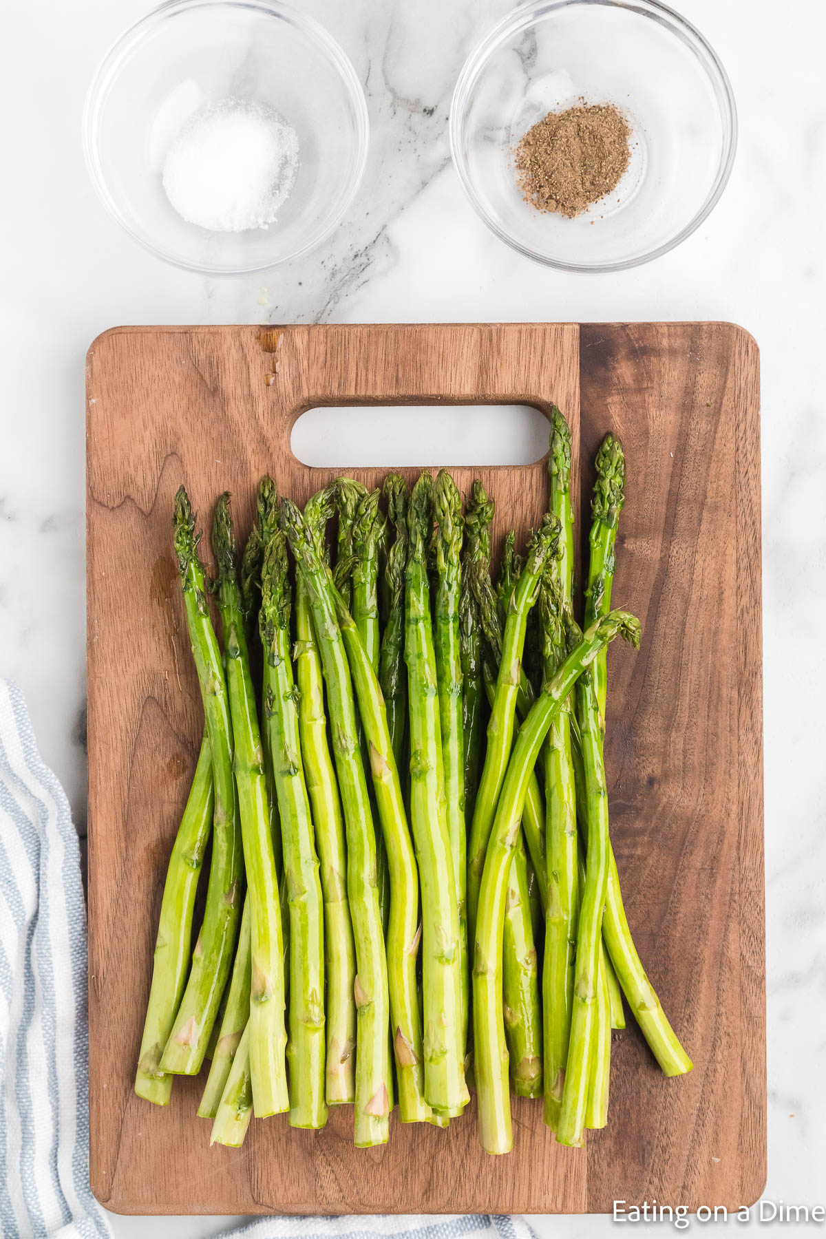 Asparagus on a cutting board with bowls of salt and pepper