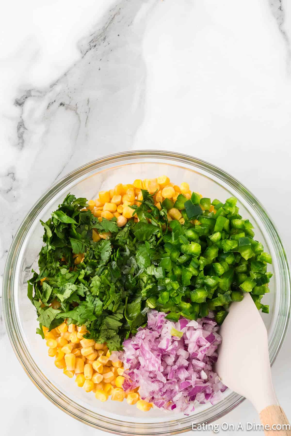 Corn kernels in the bowl topped with chopped cilantro, chopped red onions and bell peppers