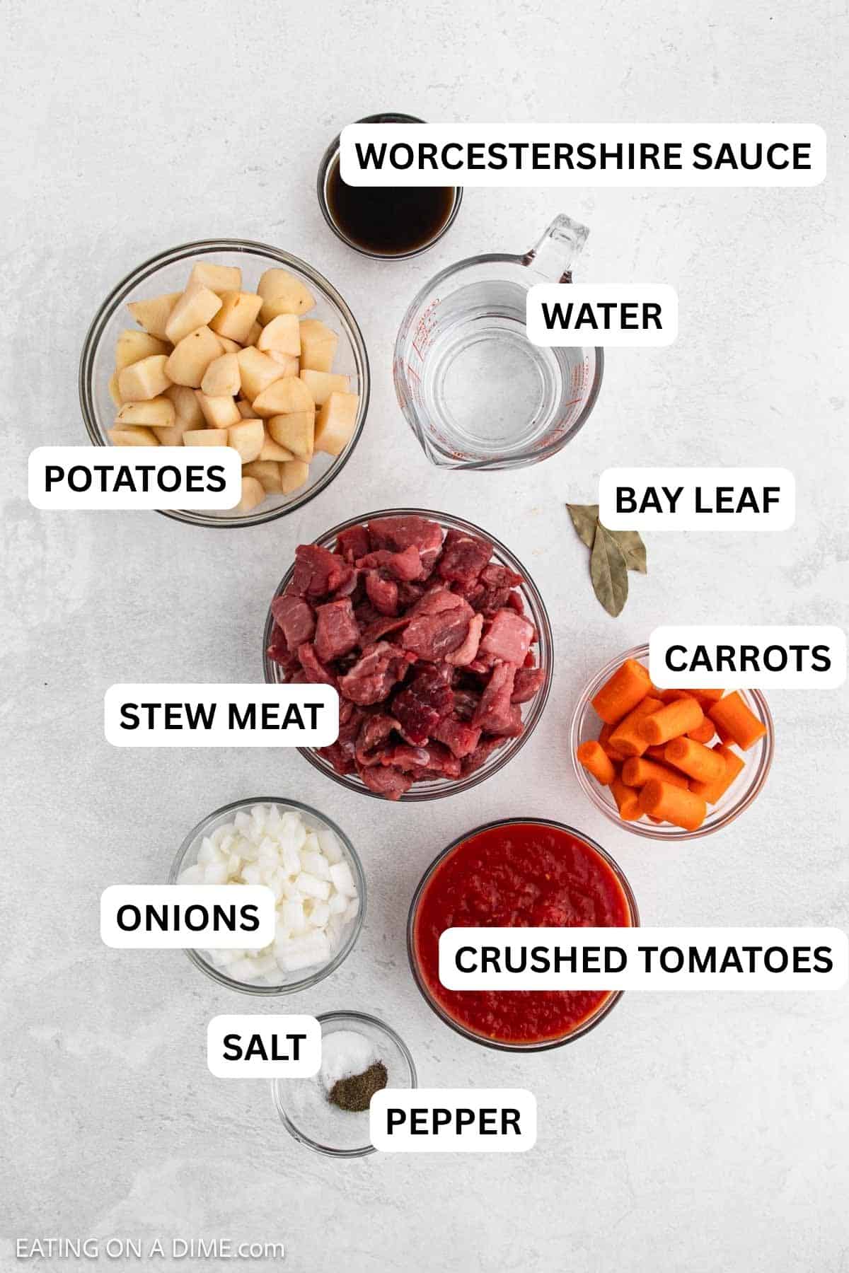 Ingredients needed for this recipe which includes diced potatoes, diced beef, chopped carrots, diced onions, seasonings, a measuring cup of water, soy sauce, bay leaves, and crushed tomatoes.