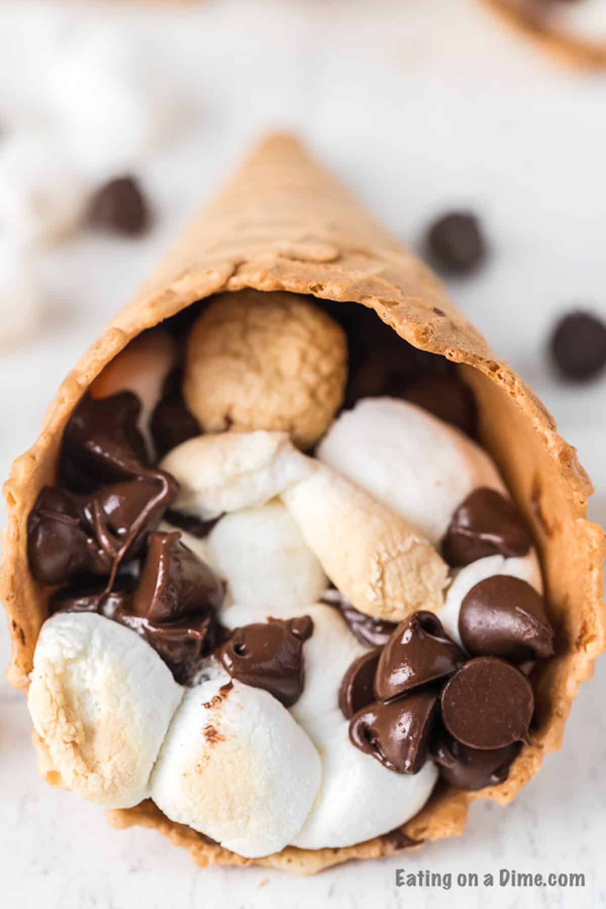 Check out how to make s’mores campfire cones that are fun and less messy than traditional s’mores. Camp fire cones are a blast and fun to make. Campfire sugar cone s’mores are a fun and easy dessert for any camping treat. Campfire s’mores cones will be your favorite summer treat! #eatingonadime #smoresrecipes #campfirecones #easydesserts