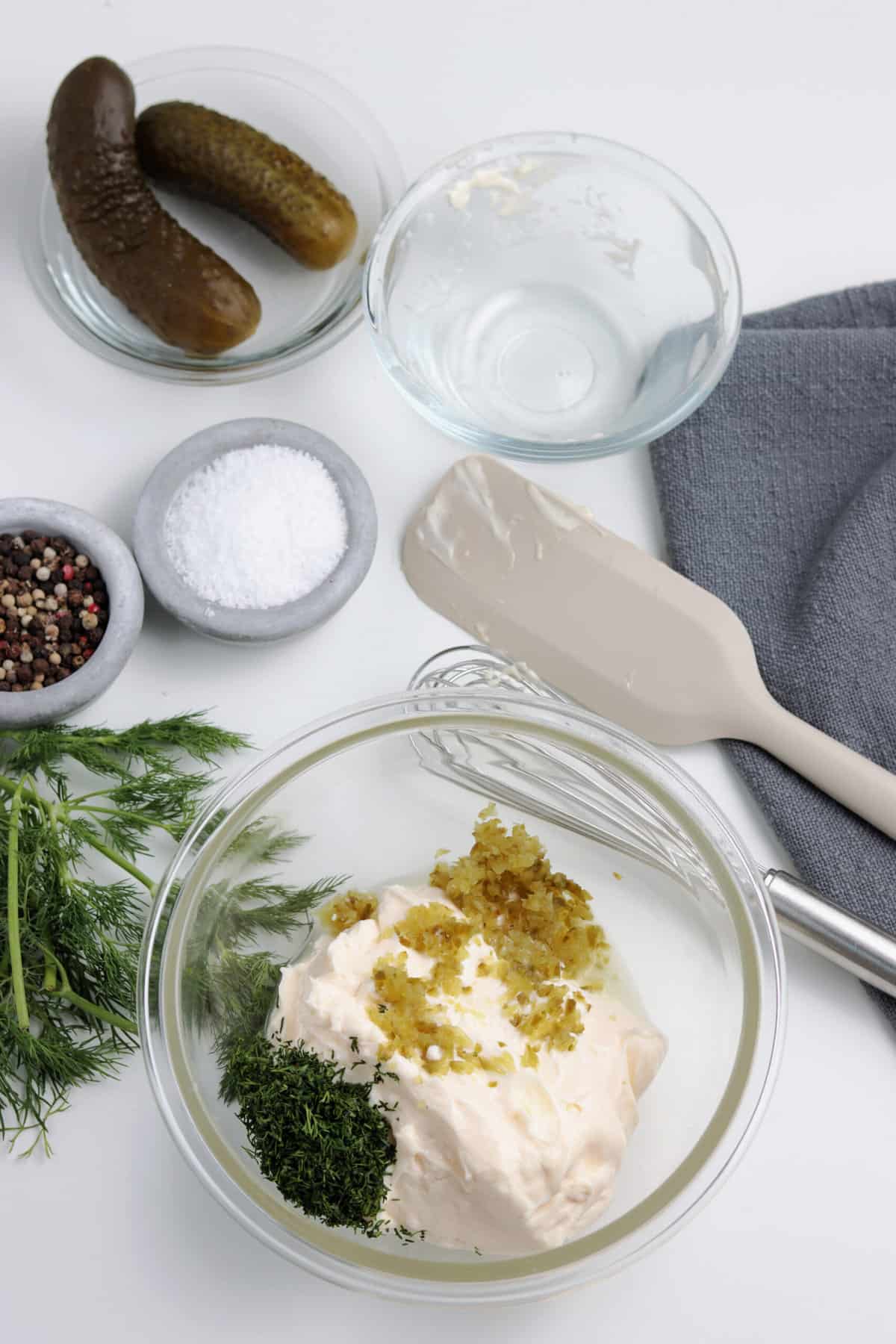 Adding the ingredients to the bowl with a bowl of pickles, salt and pepper on the side