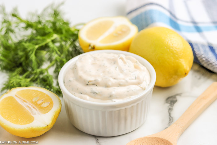 Overview of tartar sauce in a white bowl with lemons on the side. 