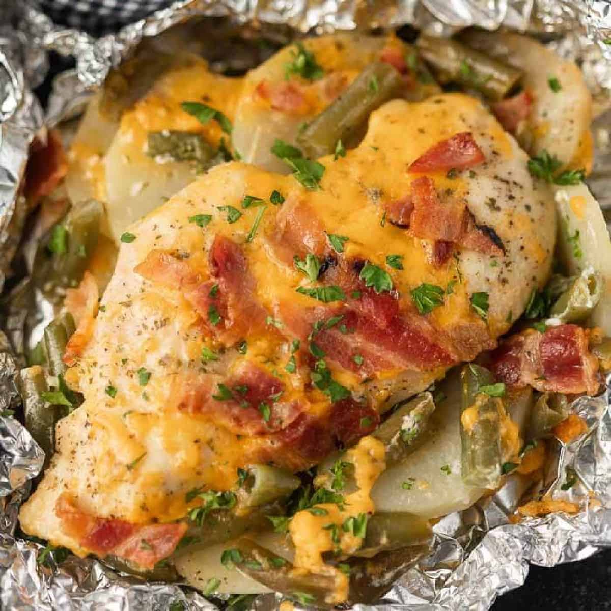 Cooked chicken breast in foil topped with diced bacon, melted cheese green beans and slice potatoes