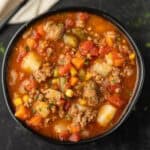 A bowl of hearty Crockpot Vegetable Beef Soup filled with ground beef, potatoes, carrots, corn, green beans, and tomatoes in a rich, red broth, garnished with fresh herbs.