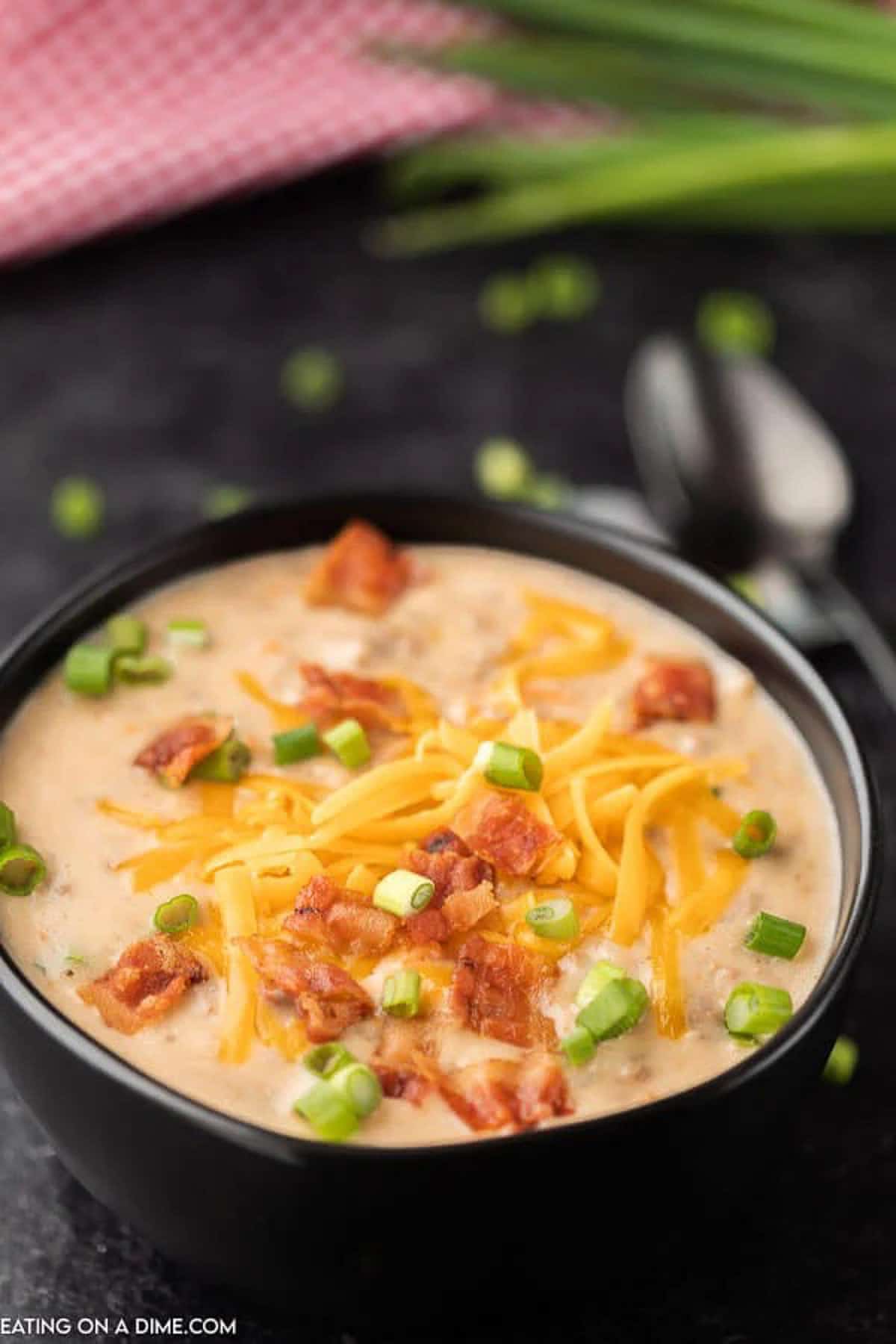 Crock Pot Cheeseburger soup in a black bowl topped with shredded cheddar cheese, diced bacon and diced green onions. 
