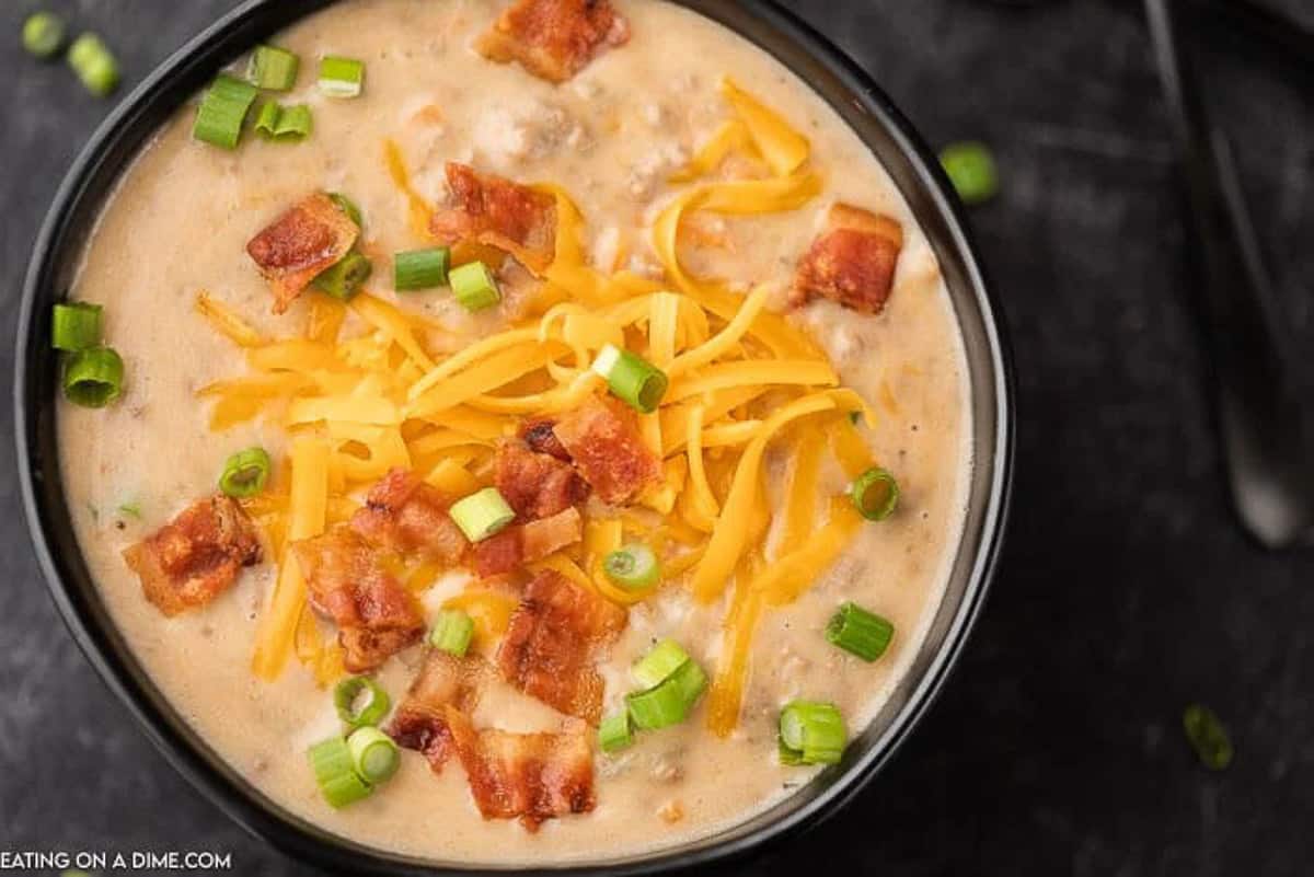 Crock Pot Cheeseburger soup in a black bowl topped with shredded cheddar cheese, diced bacon and diced green onions. 