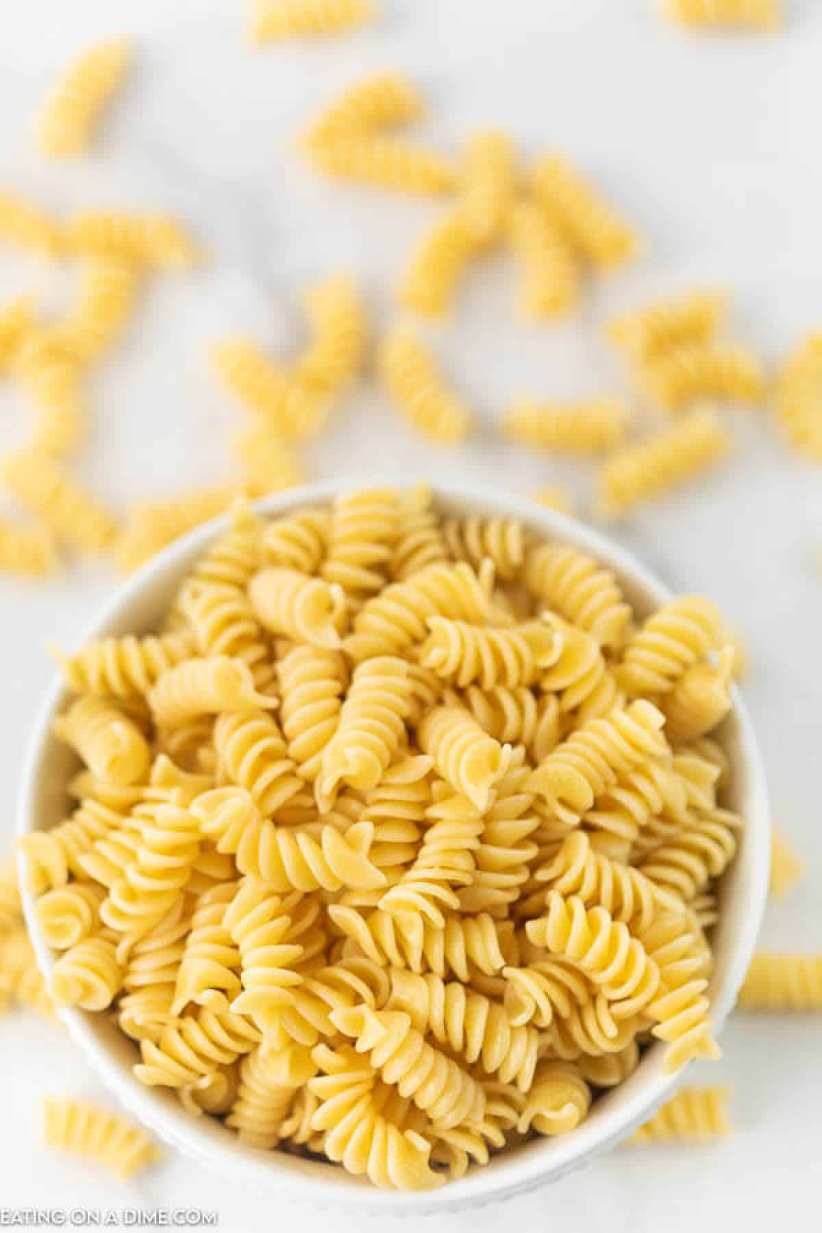 An overview of cooked rotini pasta in a bowl and some scattered on a countertop.