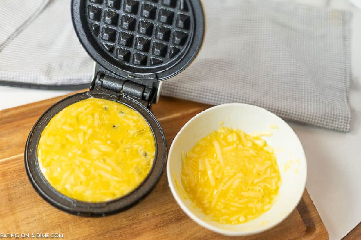 Egg mixture poured into the mini waffle maker with a bowl of the mixture on the side.