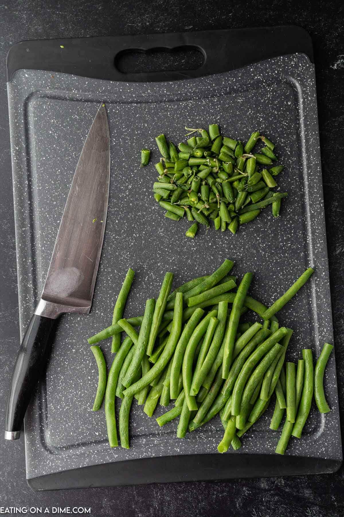 Green beans being trimmed on a cutting board with a sharp knife