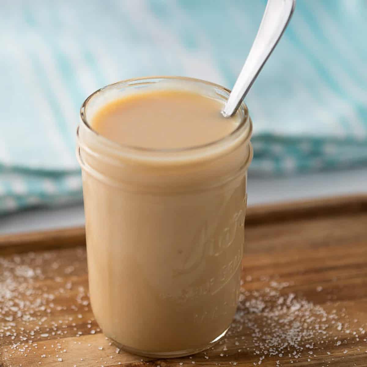 Homemade sweetened condensed milk in a mason jar with a spoon