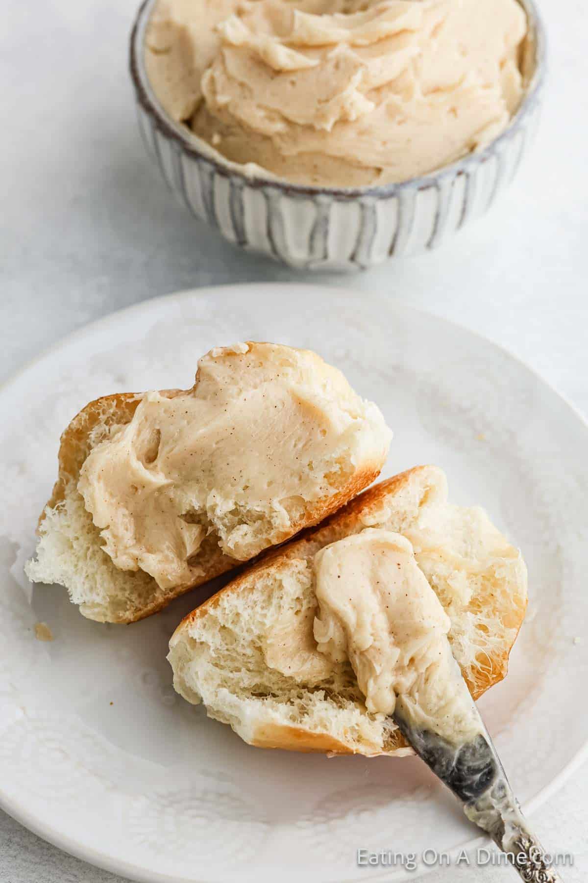 Cinnamon Butter topped on a roll that is cut in half on a plate with a small bowl of cinnamon butter on the side