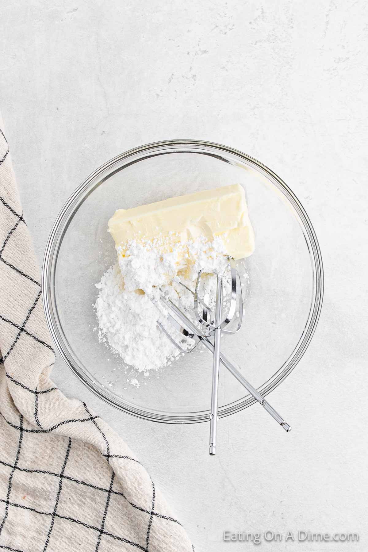 Cream cheese and powdered sugar in a bowl with hand mixers