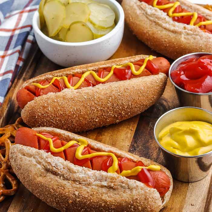 Close up of multiple hot dogs on a wooden platter topped with ketchup and mustard 