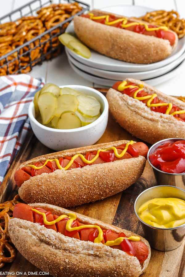 Hot dogs on a wooden platter with ketchup, mustard, pickles and pretzels on the platter.  