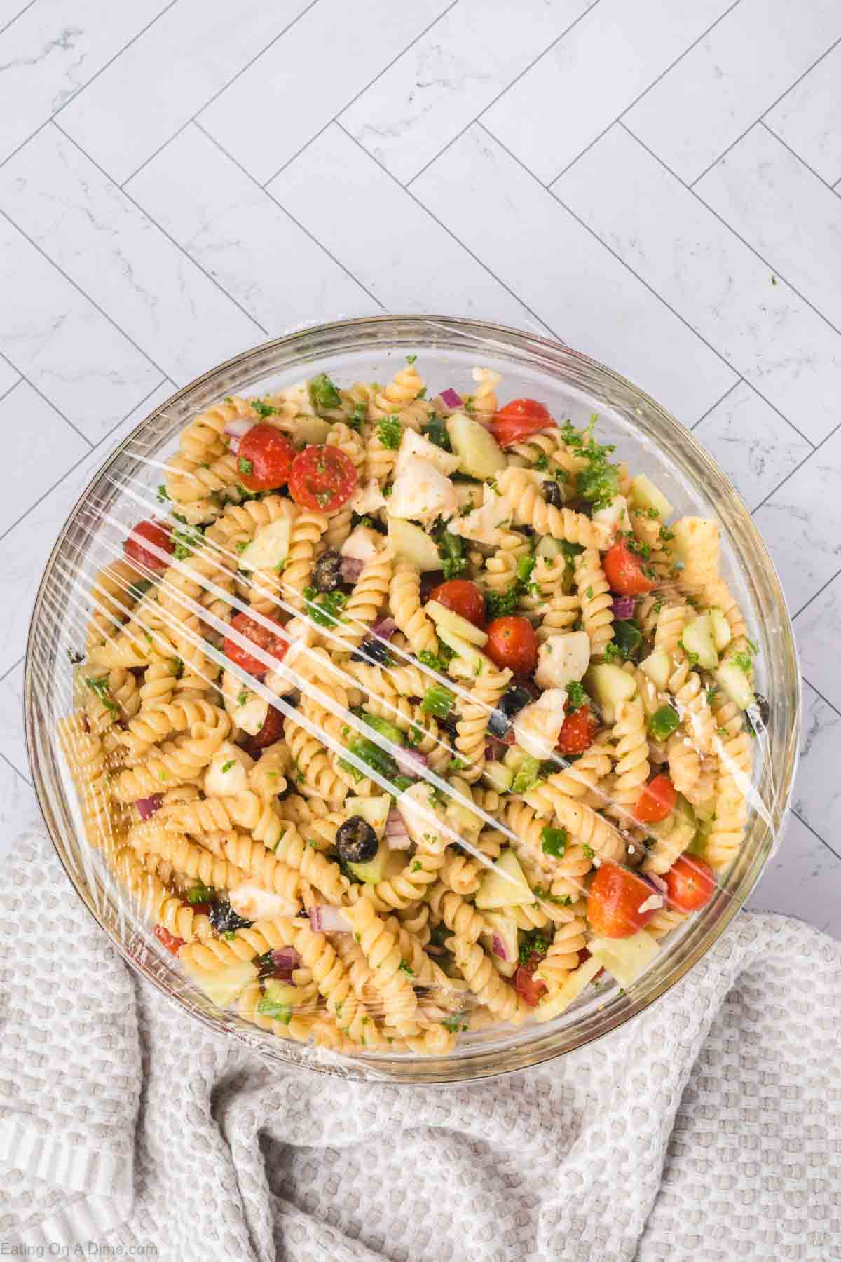 Pasta salad covered with plastic wrap in a bowl