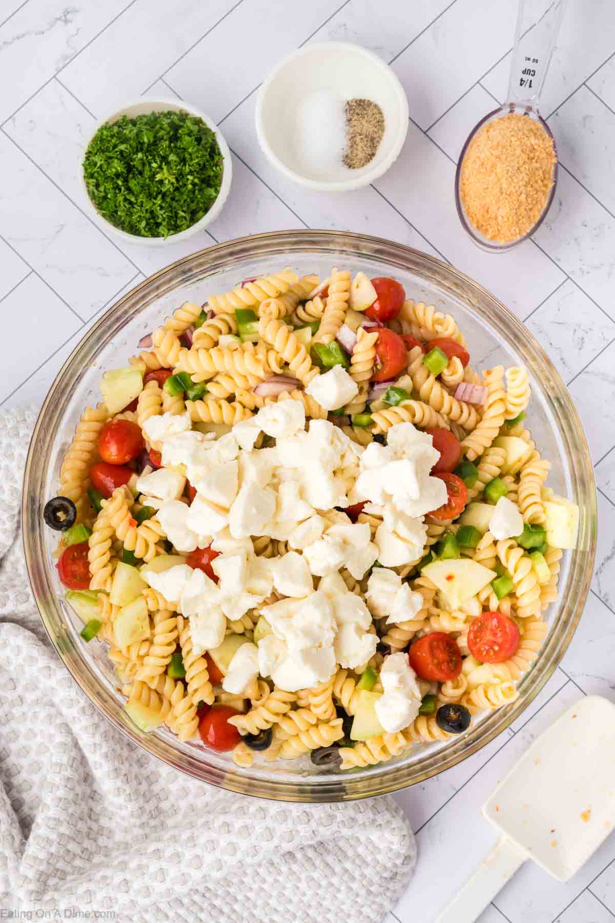 Adding the cooked pasta to a bowl and adding in the cherry tomatoes, black olives, green peppers and the mozzarella balls