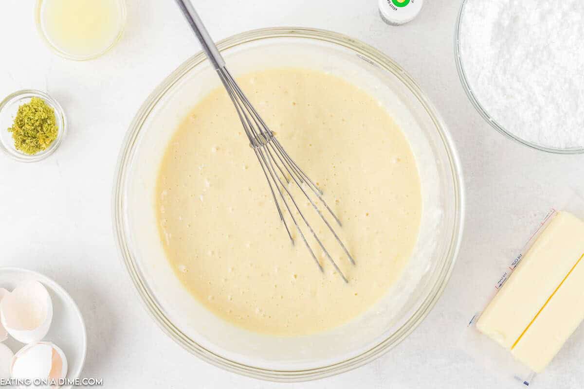 Cupcake Batter in a bowl with a whisk and two sticks of butter, powdered sugar in a bowl on the side