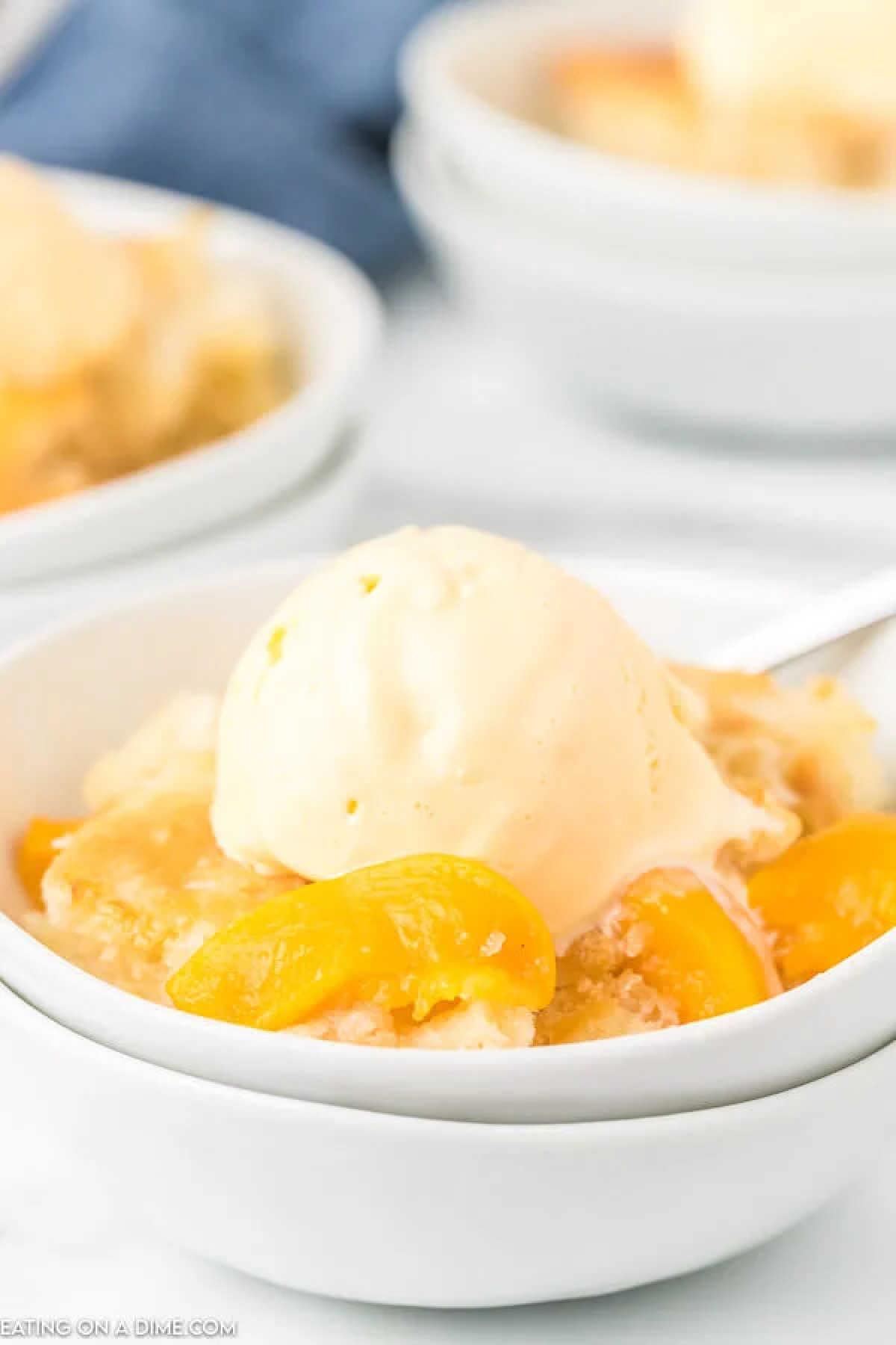 Come home to the best Crock pot peach cobbler recipe all ready to enjoy. The slow cooker does all of the work and we love it with ice cream.ย A delicious crock pot peach cobbler topped with a scoop of vanilla ice cream sits invitingly in a white bowl. The dessert showcases juicy peach slices and a crumbly texture, while a spoon is partially visible beside the bowl, ready for you to savor each bite.