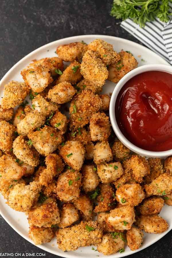 A large plate of chicken nuggets with a small bowl of ketchup next to them. 