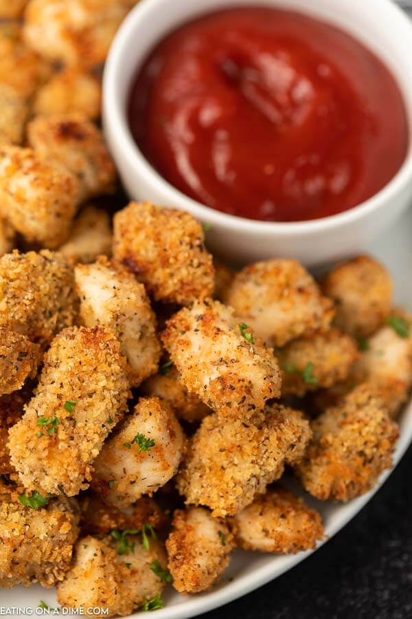 Close up of air fried chicken nuggets on a white plate with a bowl of ketchup. 