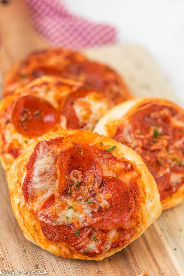 4 pepperoni pizzas stacked on a wooden platter. 