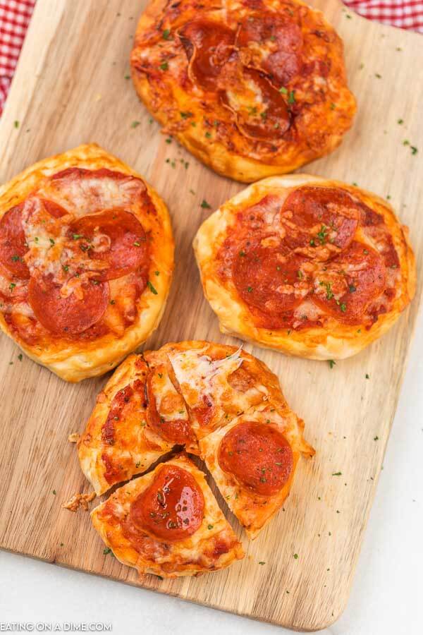 Cooked mini pepperoni pizzas on a wooden board and one of the pizzas is cut into 4 even pieces. 