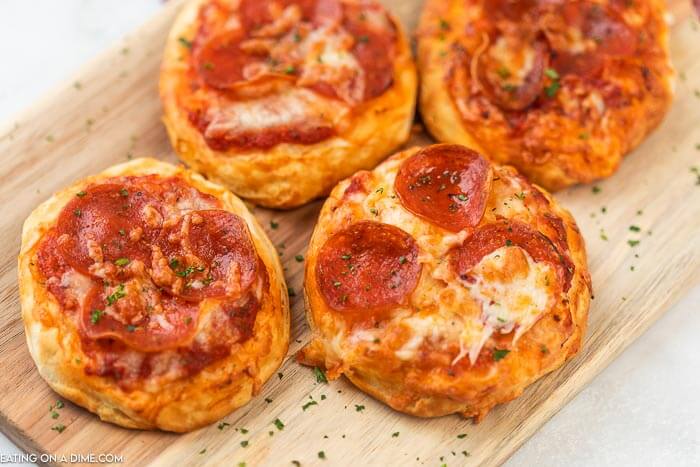 4 mini air fryer pepperoni pizzas on a wooden platter with parsley sprinkled on top. 