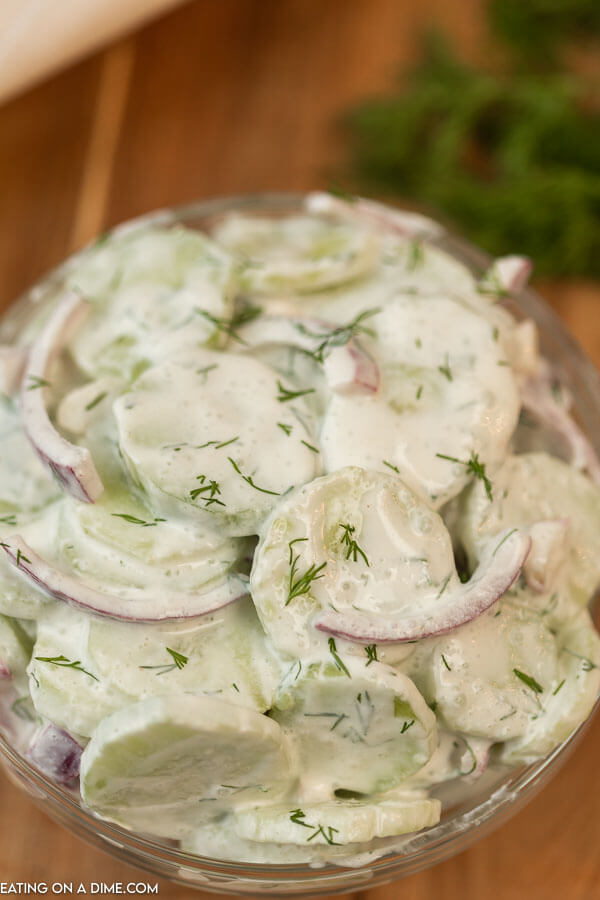 Creamy Cucumber and Red Onion Salad in a Clear Bowl with fresh parsley behind it 
