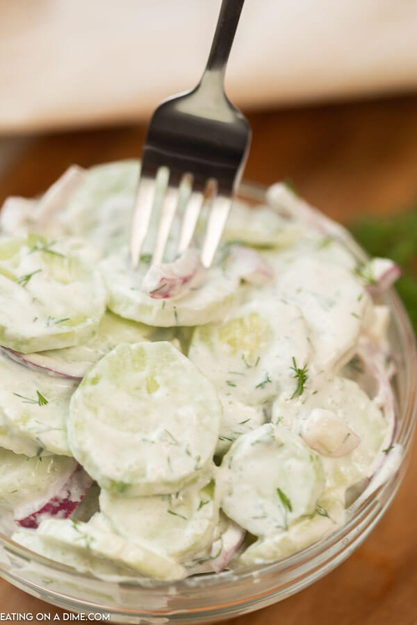 Creamy Cucumber and Red Onion Salad in a Clear Bowl with a fork taking a piece out of it 