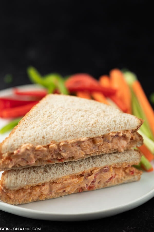 A full size pimento cheese sandwich on a white plate with sliced veggies next to it 