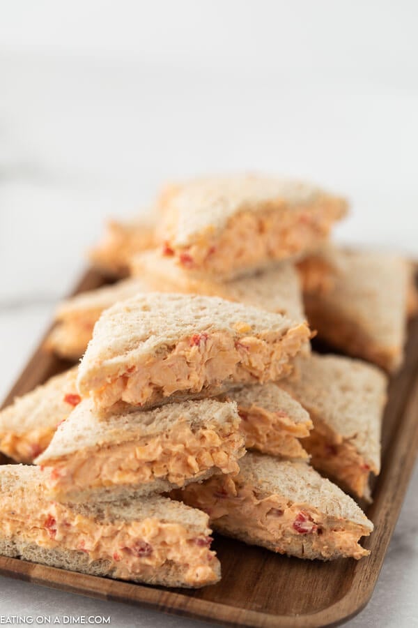 Small tea size pimento cheese sandwiches stacked on top of each other a wooden platter 