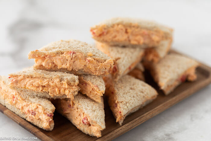 Small Pimento Cheese Sandwiches on a wooden platter on a white countertop 