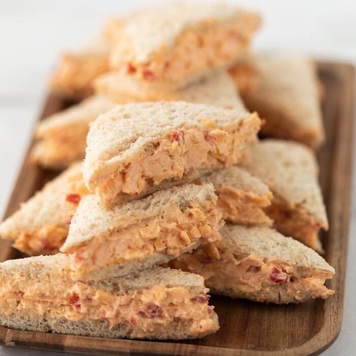 Small pimento cheese sandwiches on a wooden platter - a perfect appetizer! 