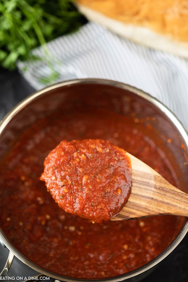 A large wooden spoon scooping marinara sauce out of a metal saucepan. 
