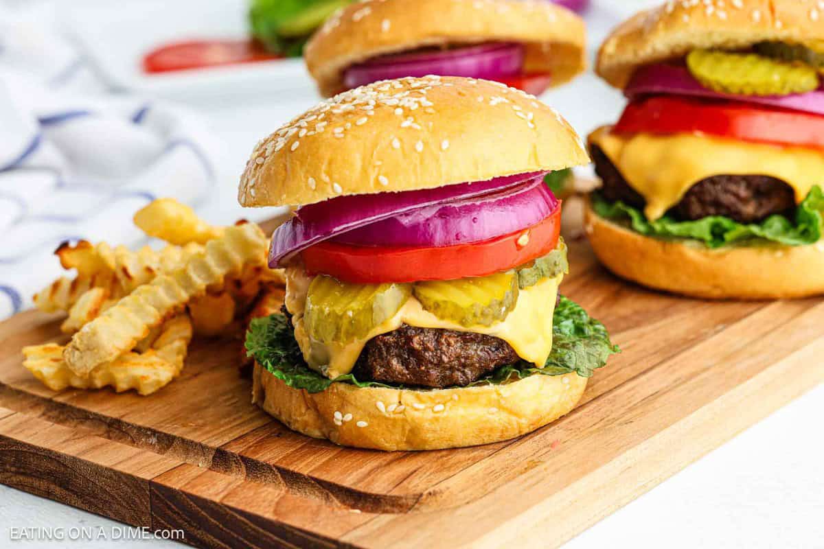 Air fryer hamburgers on a cutting board with crinkle cut fries on the side.