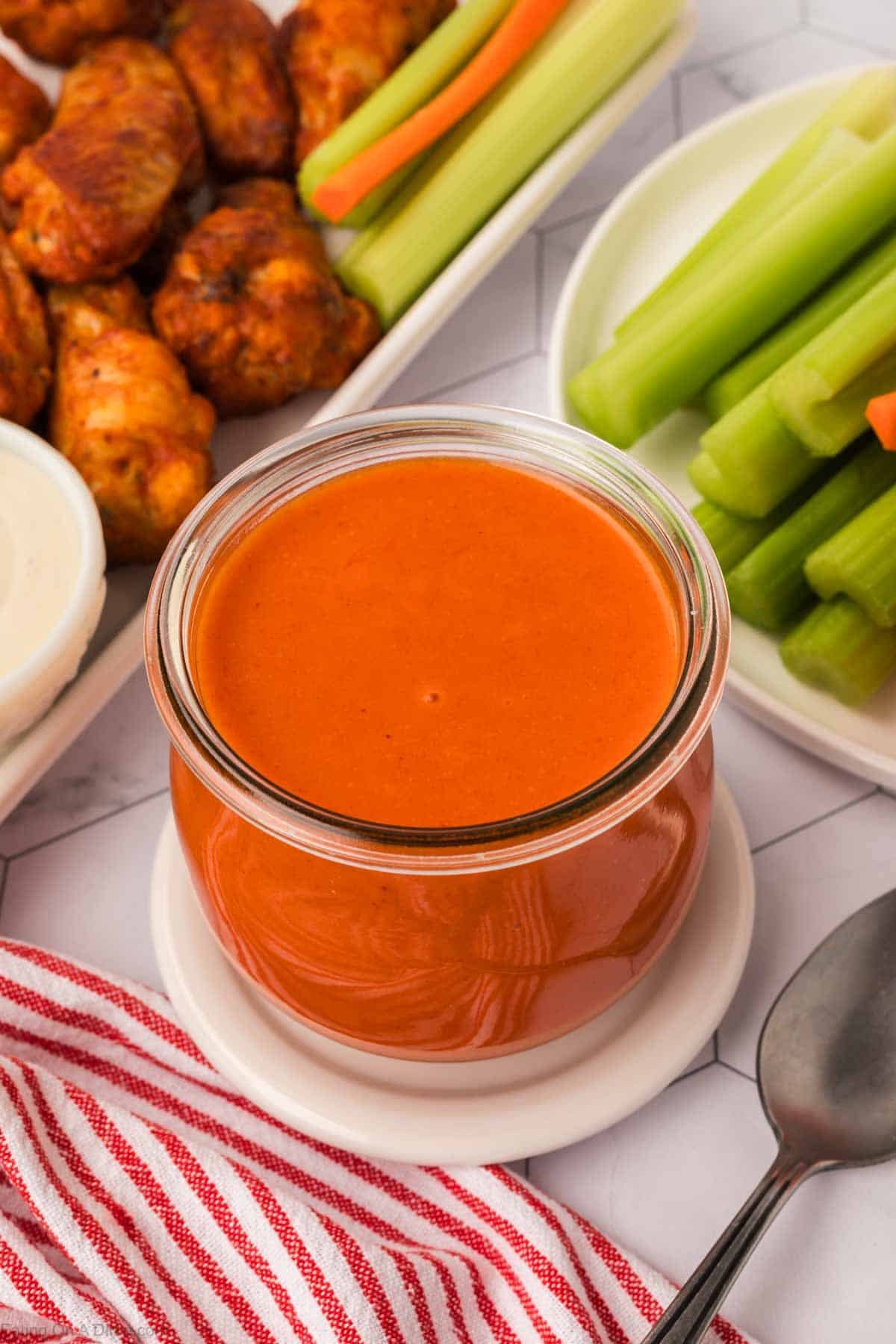 Sauce in a jar with celery and wings on a platter nearby.
