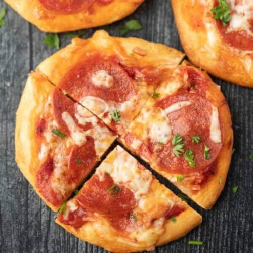 A small biscuit pizza recipe topped with pepperoni, melted cheese, and chopped parsley, cut into four slices and placed on a dark wooden surface.