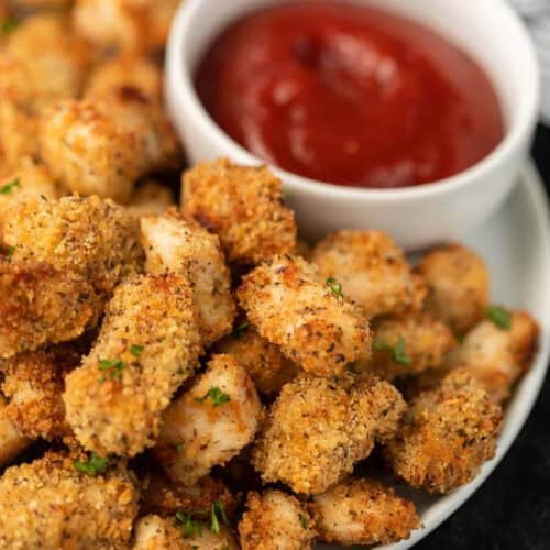 air fried chicken nuggets on a white plate with ketchup in the back ground.