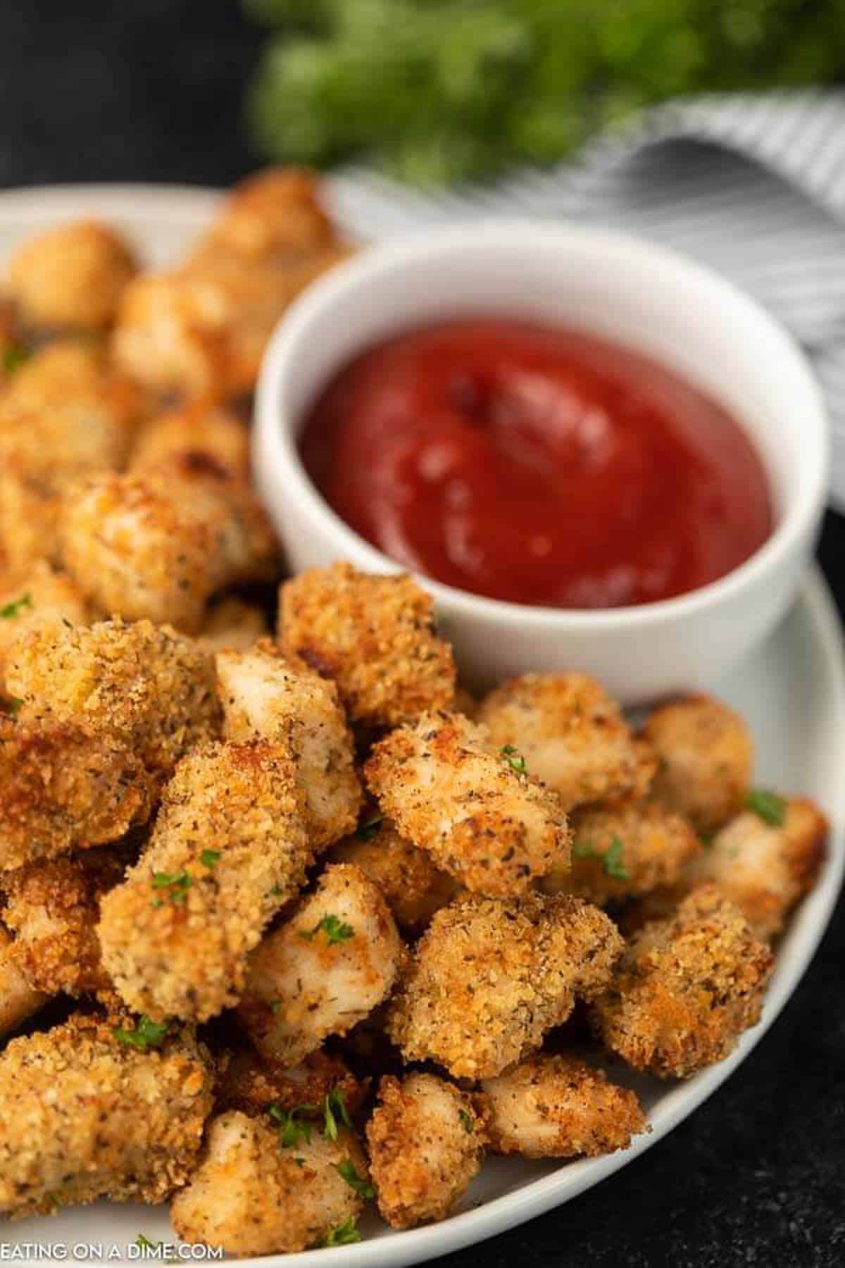 air fried chicken nuggets on a white plate with ketchup in the back ground. 