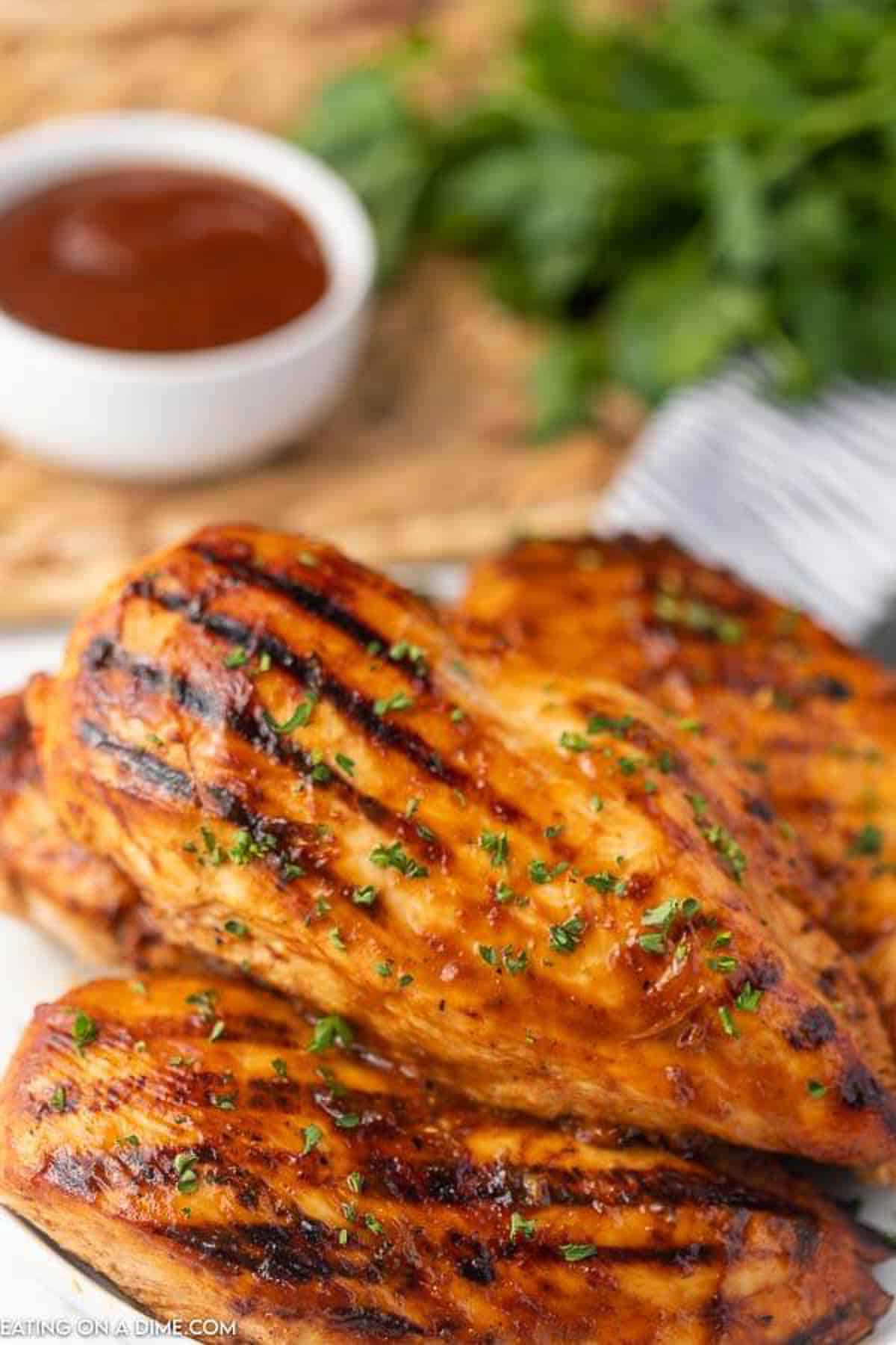 Grilled chicken on a white plate with barbecue sauce and fresh parsley in the back ground. 