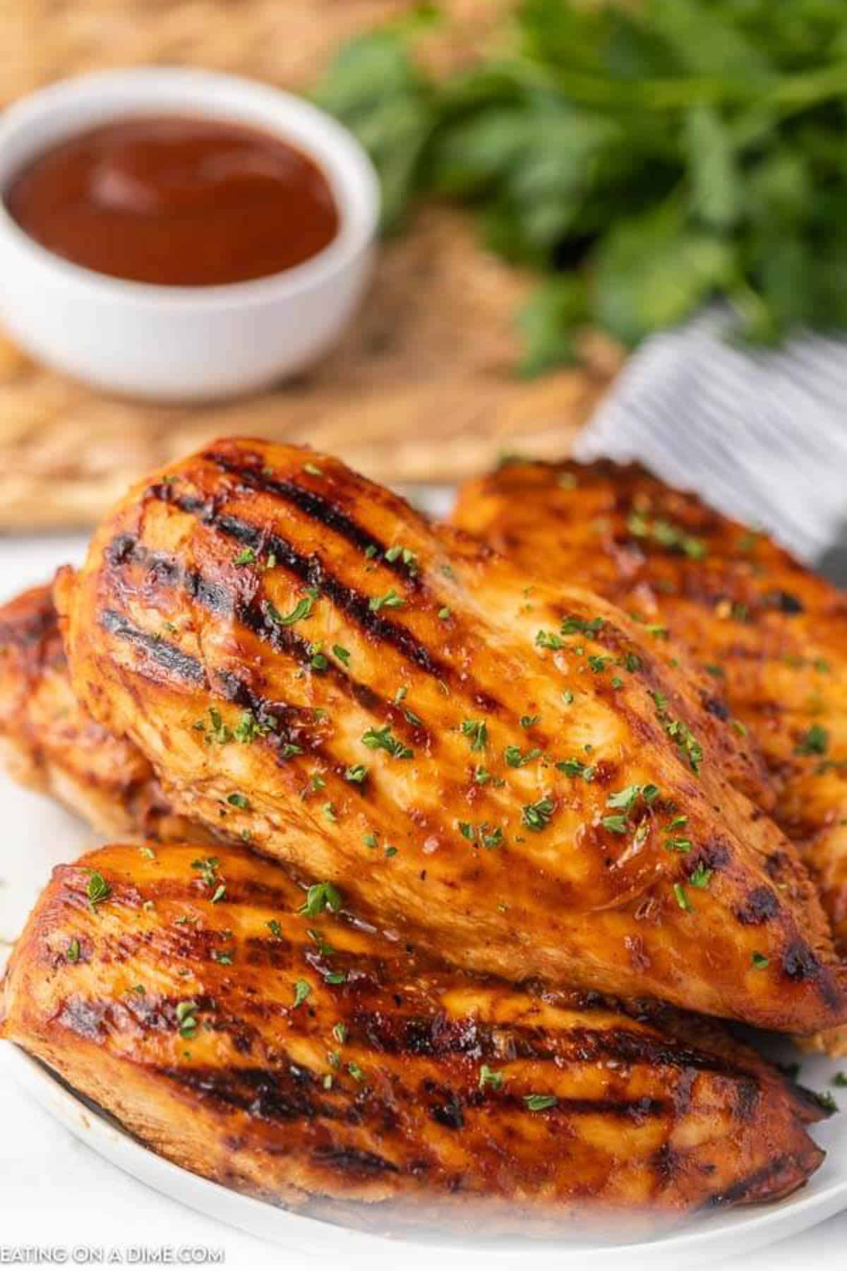 Grilled chicken on a white plate with barbecue sauce and fresh parsley in the back ground. 