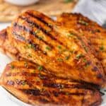 4 pieces of grilled barbecue chicken on a white plate topped with fresh parsley.