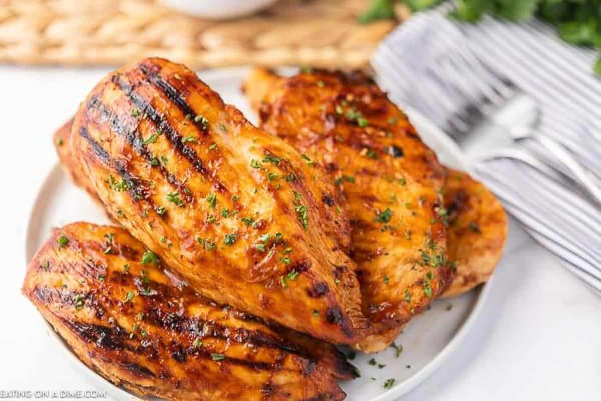 4 pieces of grilled chicken on a white plate with 2 forks next to the plate on a striped linen.