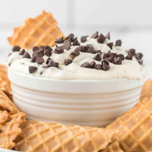 Close up image of Cannoli Dip in a white bowl with broke up cones on the side. 