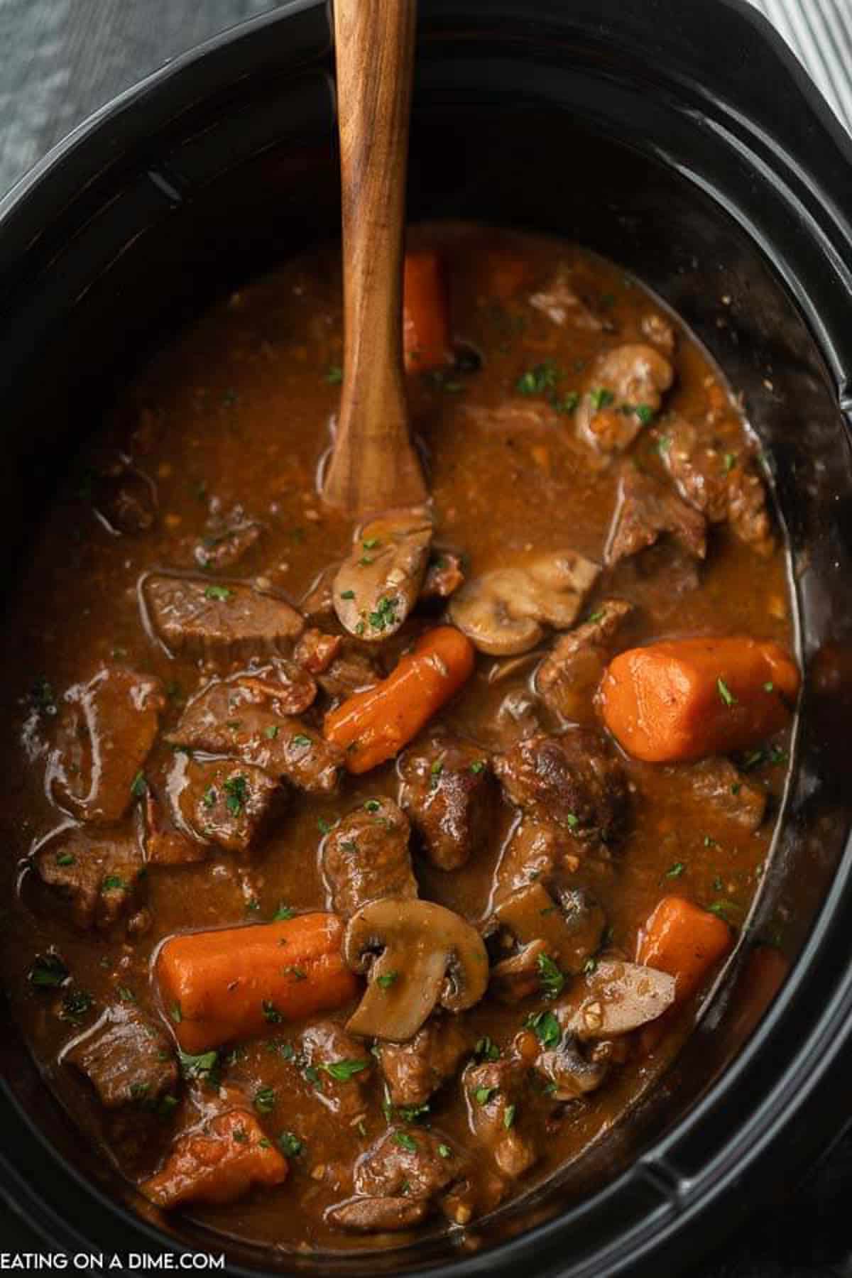 beef bourguignon in the crock pot with a wooden spoon
