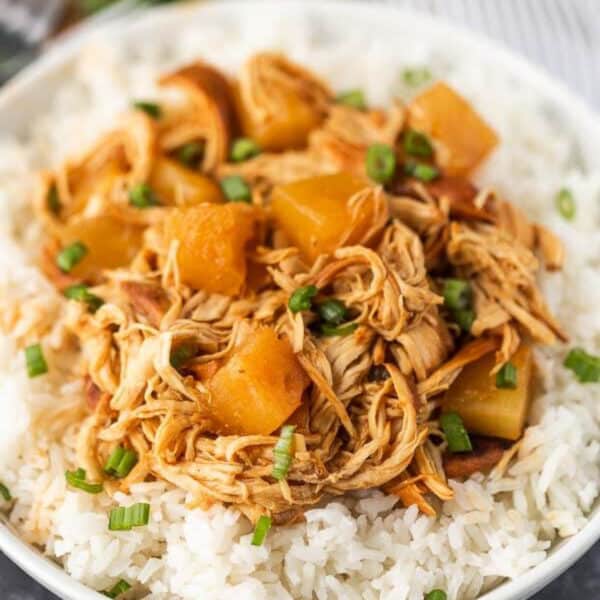 A bowl of white rice topped with crock pot Hawaiian BBQ chicken, diced pineapple, and chopped green onions.