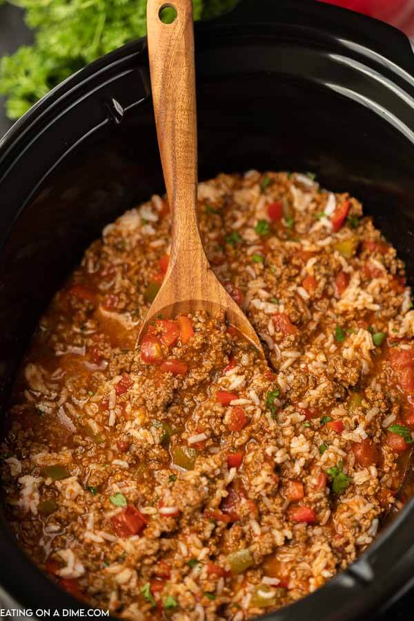 Close up image of stuffed pepper soup in a crock pot with a brown spoon.